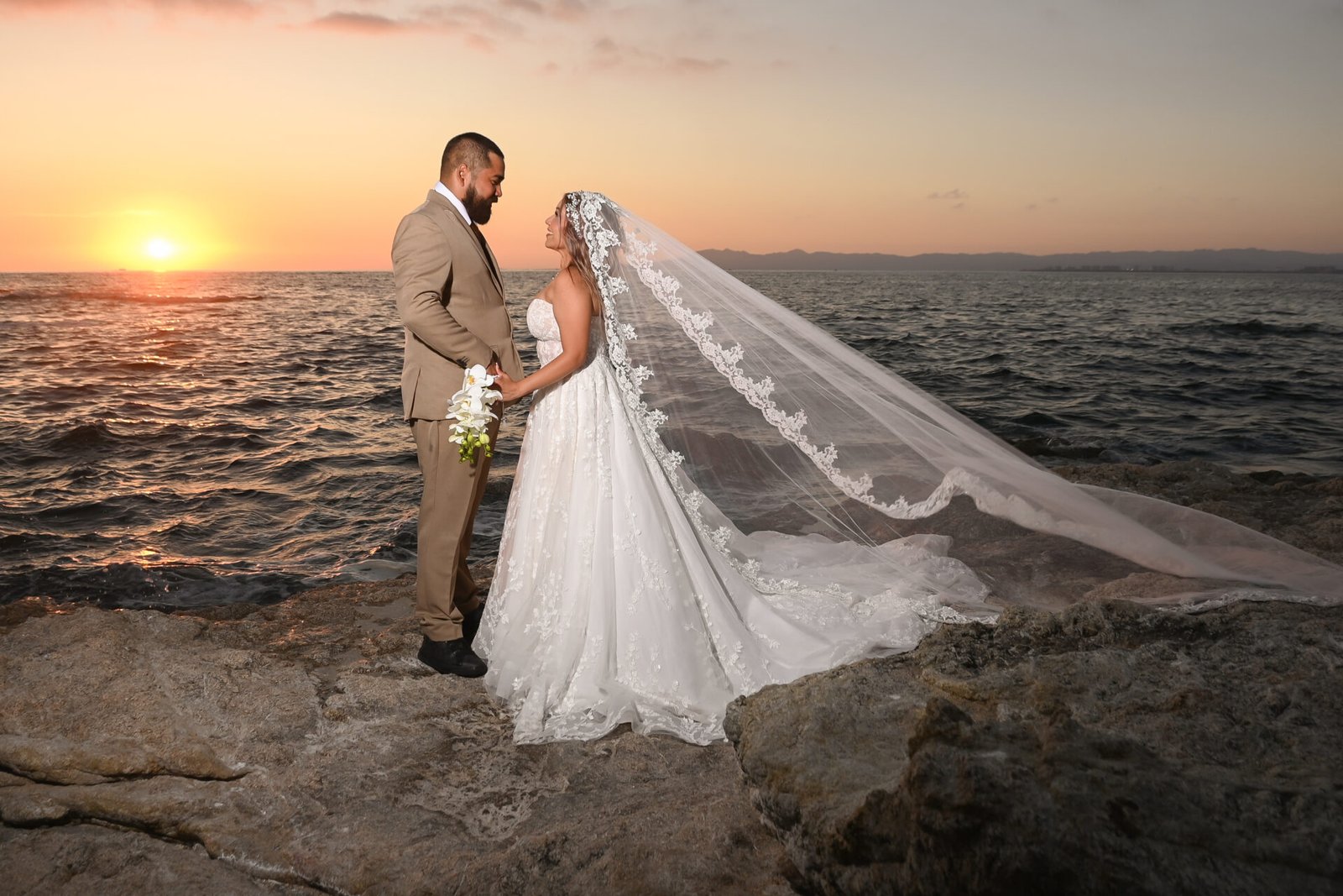 Novios junto al mar al atardecer con el velo extendido