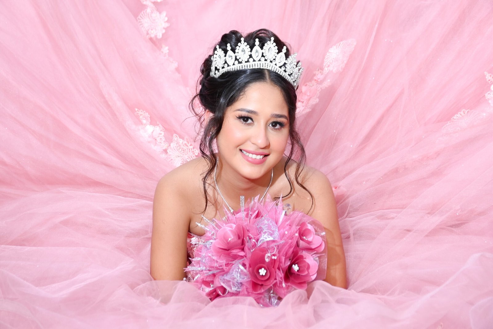 Quinceañera con vestido rosa, corona y ramo de flores