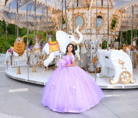Quinceañera con vestido lila junto a un carrusel