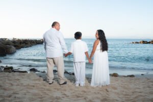 Familia de espaldas tomada de la mano frente al mar