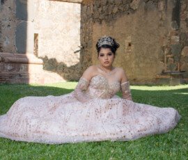 Quinceañera con vestido claro sentada en el césped