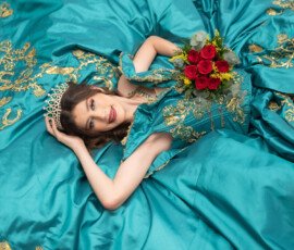 Quinceañera recostada sobre su vestido turquesa con un ramo
