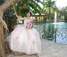 Quinceañera con vestido claro junto a un árbol