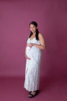 Retrato de maternidad con vestido claro sobre fondo morado