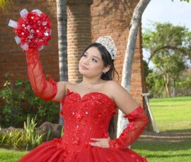 Quinceañera con vestido rojo sosteniendo un ramo en un jardín