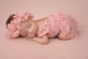 Bebé recién nacido dormido con diadema de flores y ropa rosa