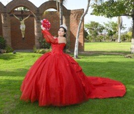 Quinceañera con vestido rojo sosteniendo un ramo en un jardín