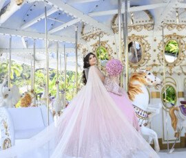 Quinceañera con vestido claro junto a un carrusel