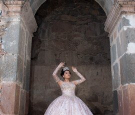 Quinceañera con vestido claro bajo un arco de piedra