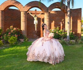 Quinceañera con vestido rosa frente a una fachada de arcos