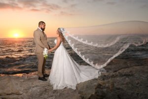 Novios junto al mar al atardecer con el velo extendido