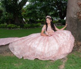 Quinceañera sentada con su vestido rosa extendido en el jardín