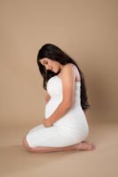 Retrato de maternidad con ropa blanca sobre fondo beige