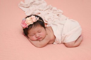 Bebé recién nacido dormido con diadema de flores y ropa rosa