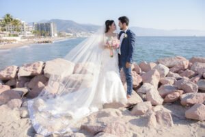 Retrato de novios junto al mar con el velo extendido