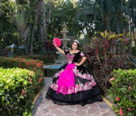 Quinceañera con vestido rosa y negro en un jardín