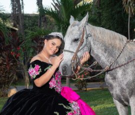 Quinceañera junto a un caballo blanco entre árboles