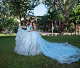 Quinceañera con vestido azul claro y cola extendida en un jardín