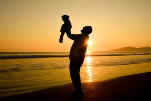 Silueta de un adulto levantando a un niño al atardecer